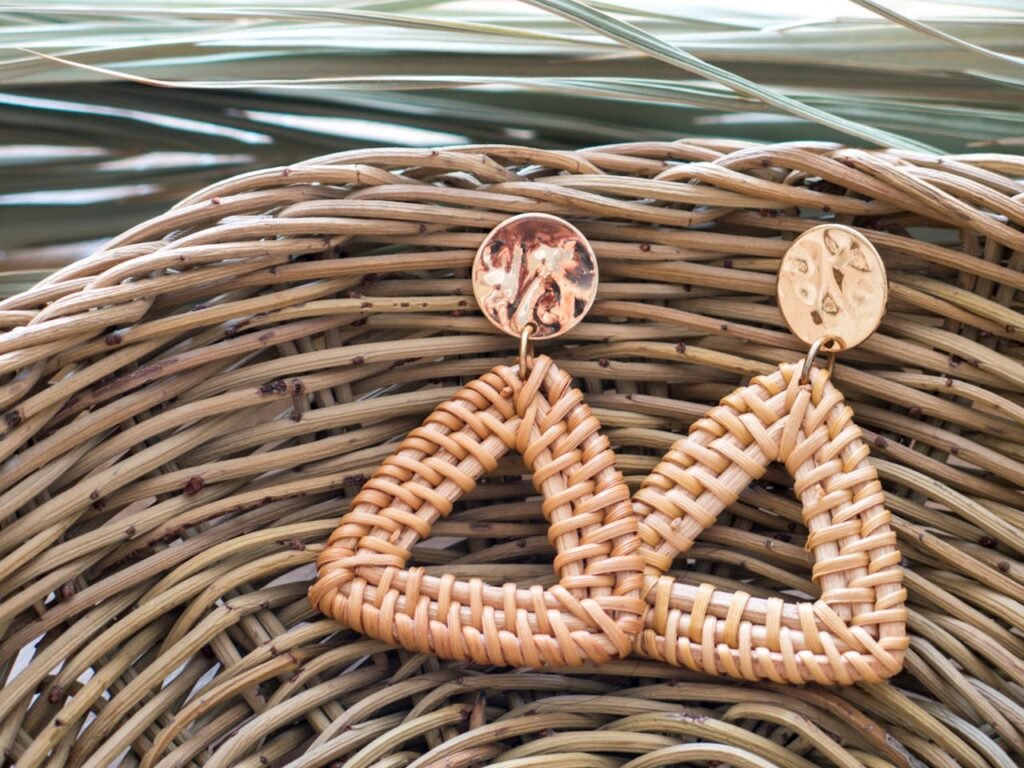 Close-up of handmade woven earrings with gold accents on a wicker basket.