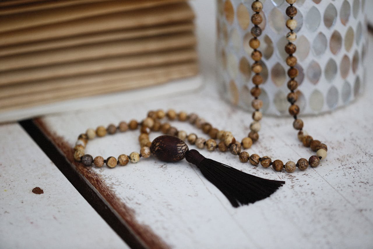 A close-up of a handmade beaded necklace with a tassel displayed on a rustic white wooden surface.