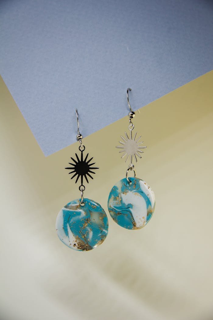 Stylish blue and white marble earrings with sun charms on paper background.